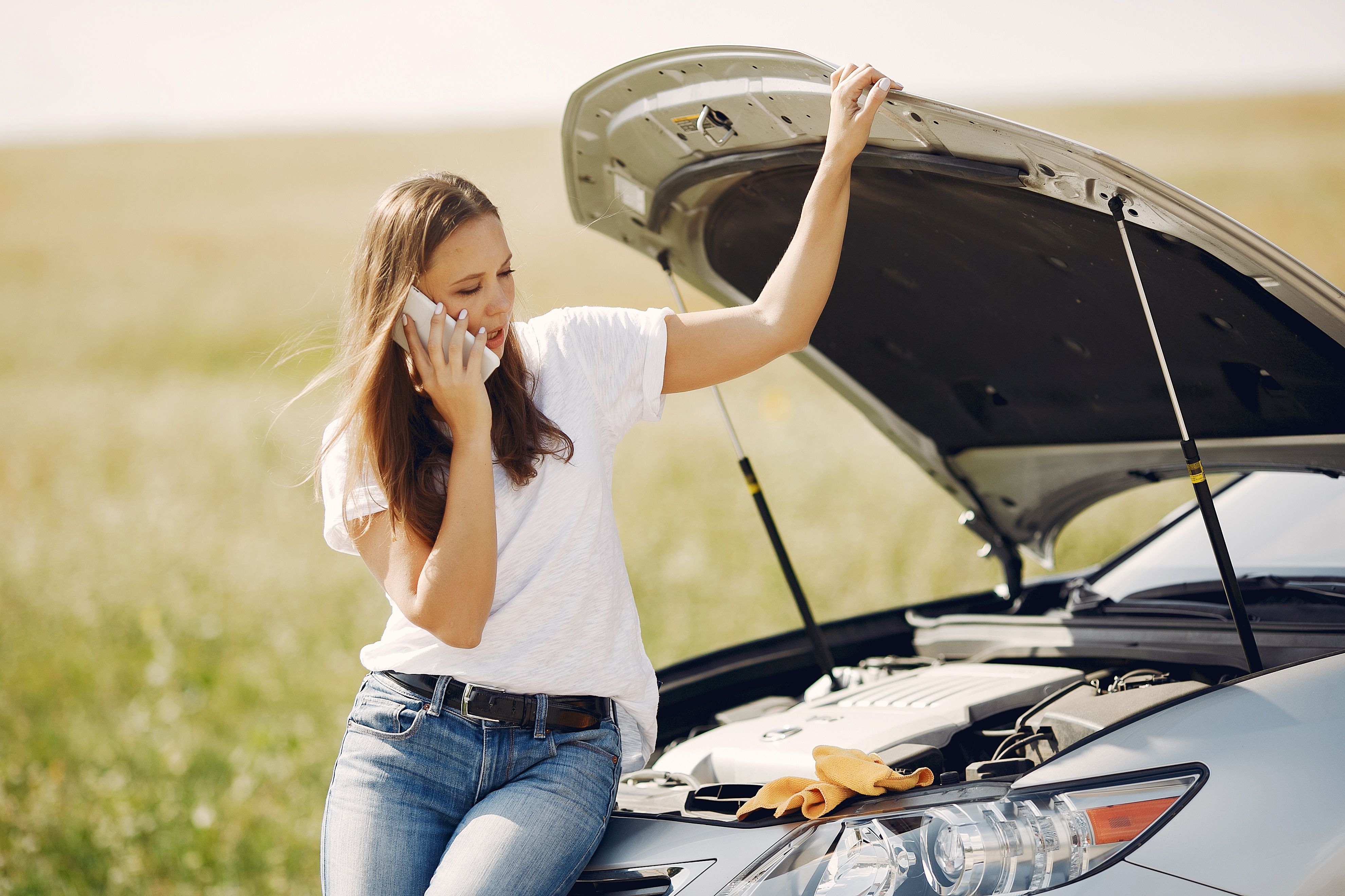 Worried driver speaking on the phone while leaning on a broken down vehicle with the hood open