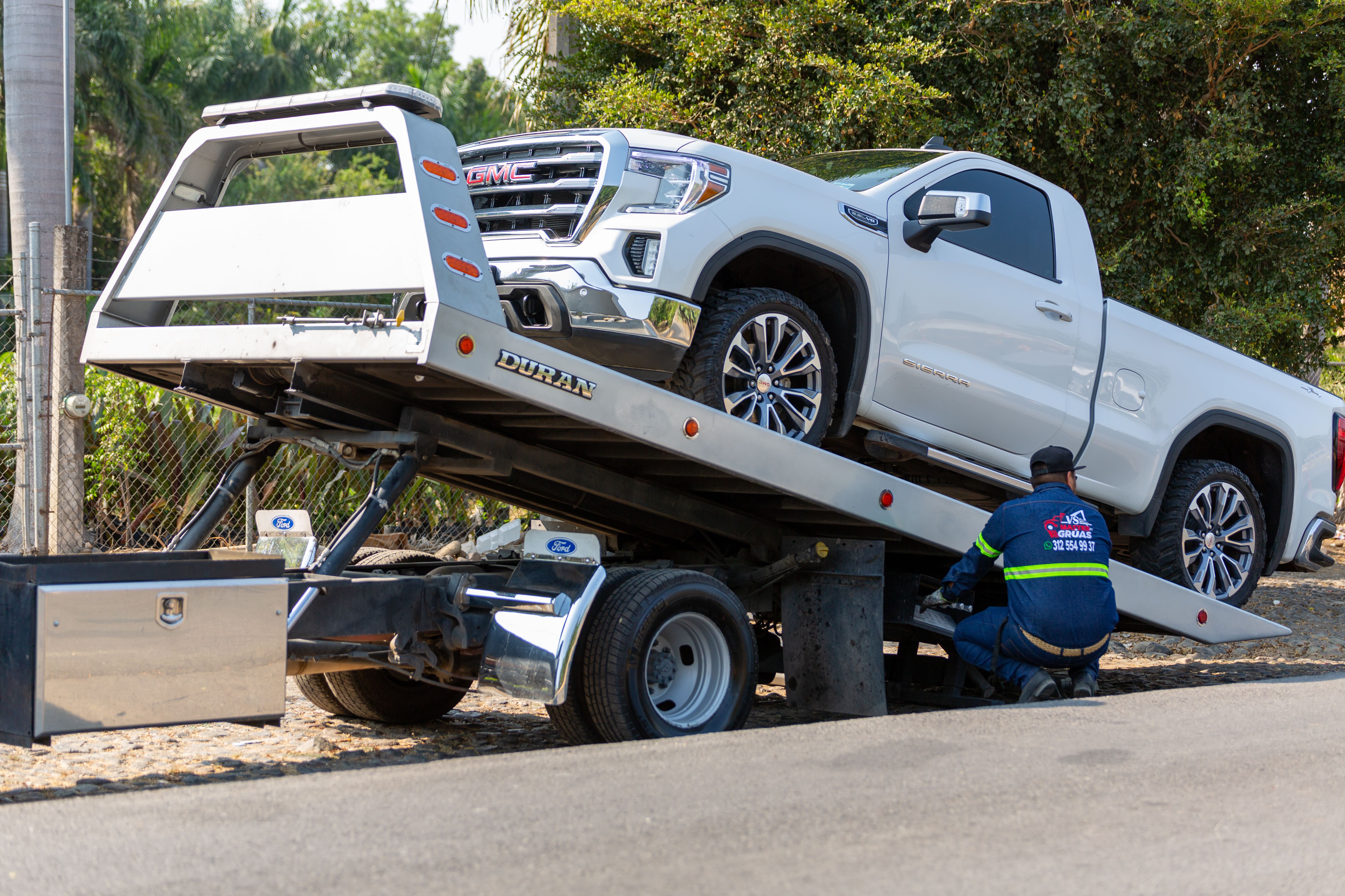 Tow truck operator loading a broken down vehicle onto a flatbed for transport