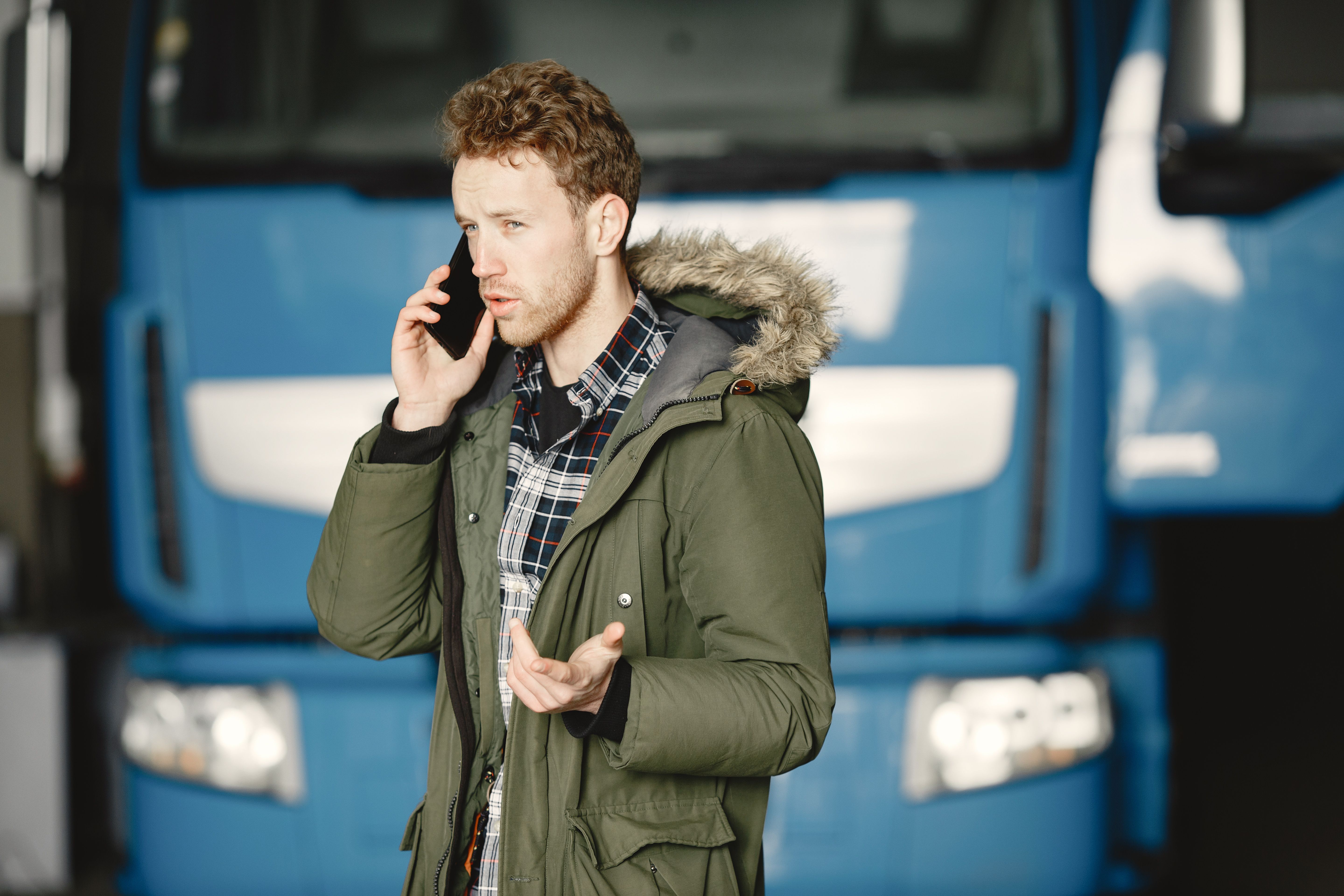 Truck driver standing outside his truck talking on the phone to call for roadside assistance