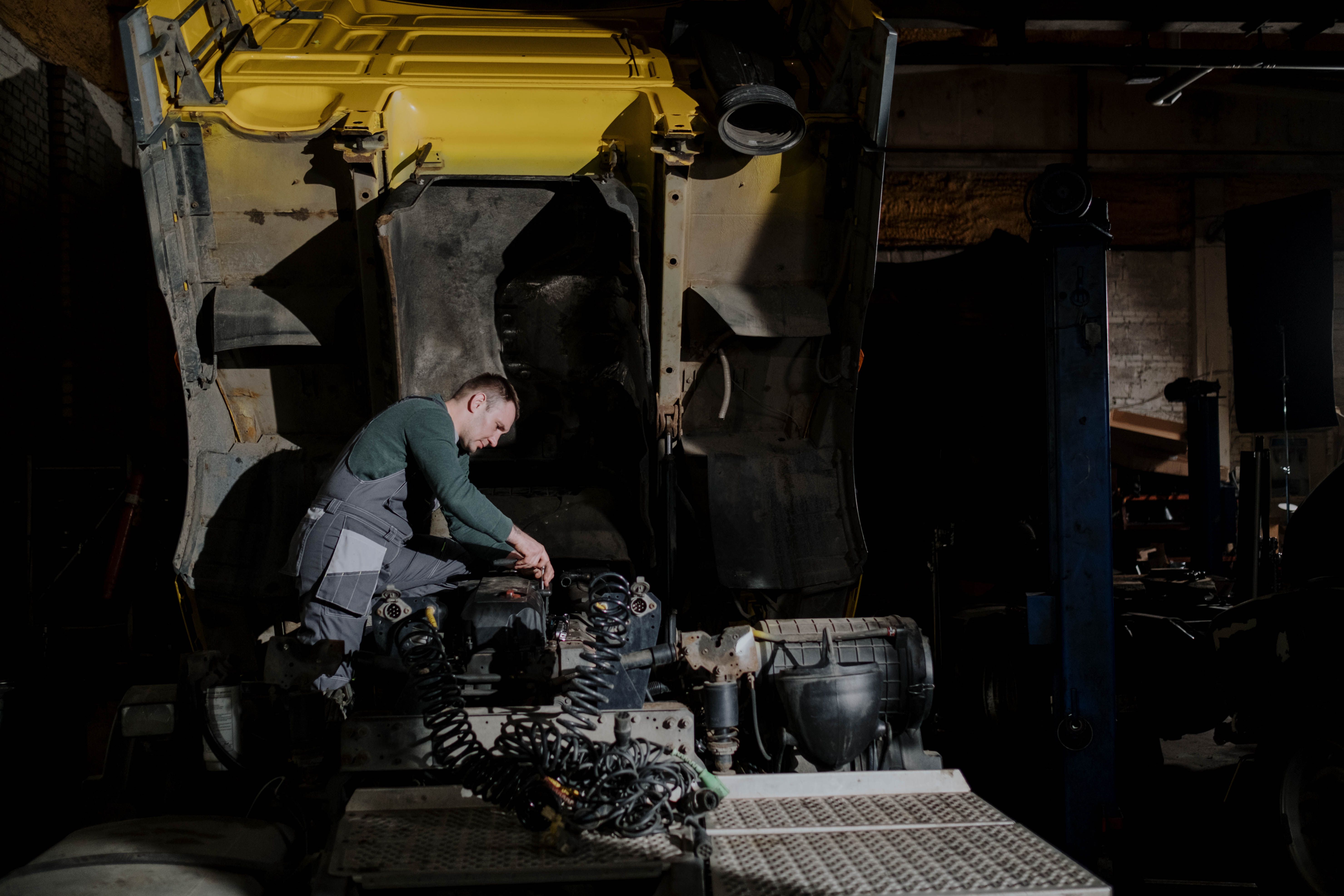Mechanic inspecting a truck engine in a dimly lit garage during a roadside repair