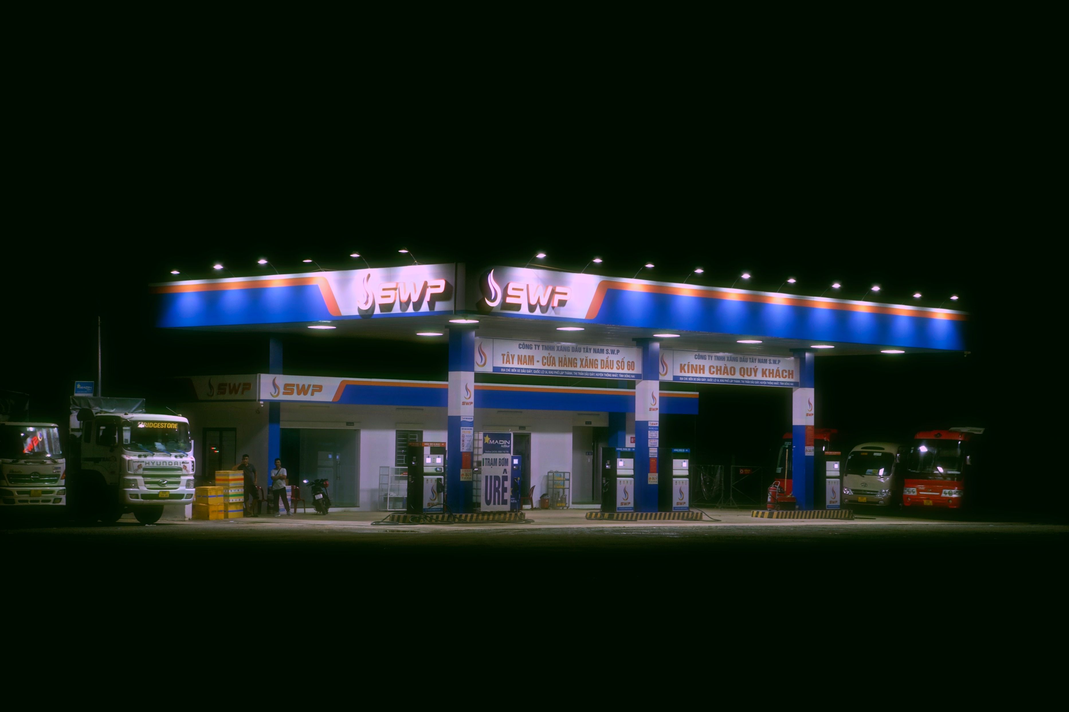 Brightly lit truck stop and gas station at night with parked trucks, a safe place to wait during a breakdown