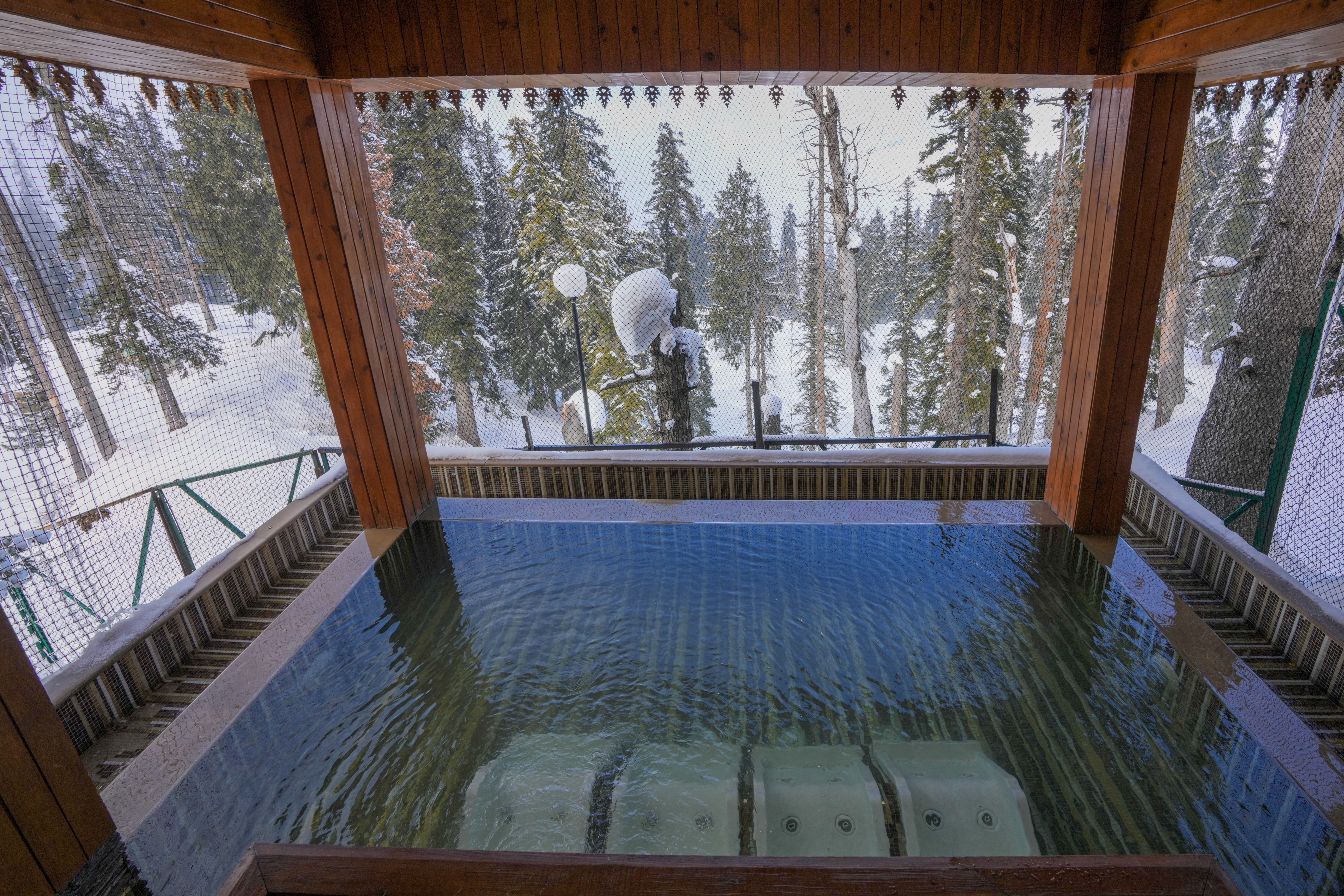 Outdoor resort pool framed by a snowy forest, evoking a winter spa retreat in the Alps.