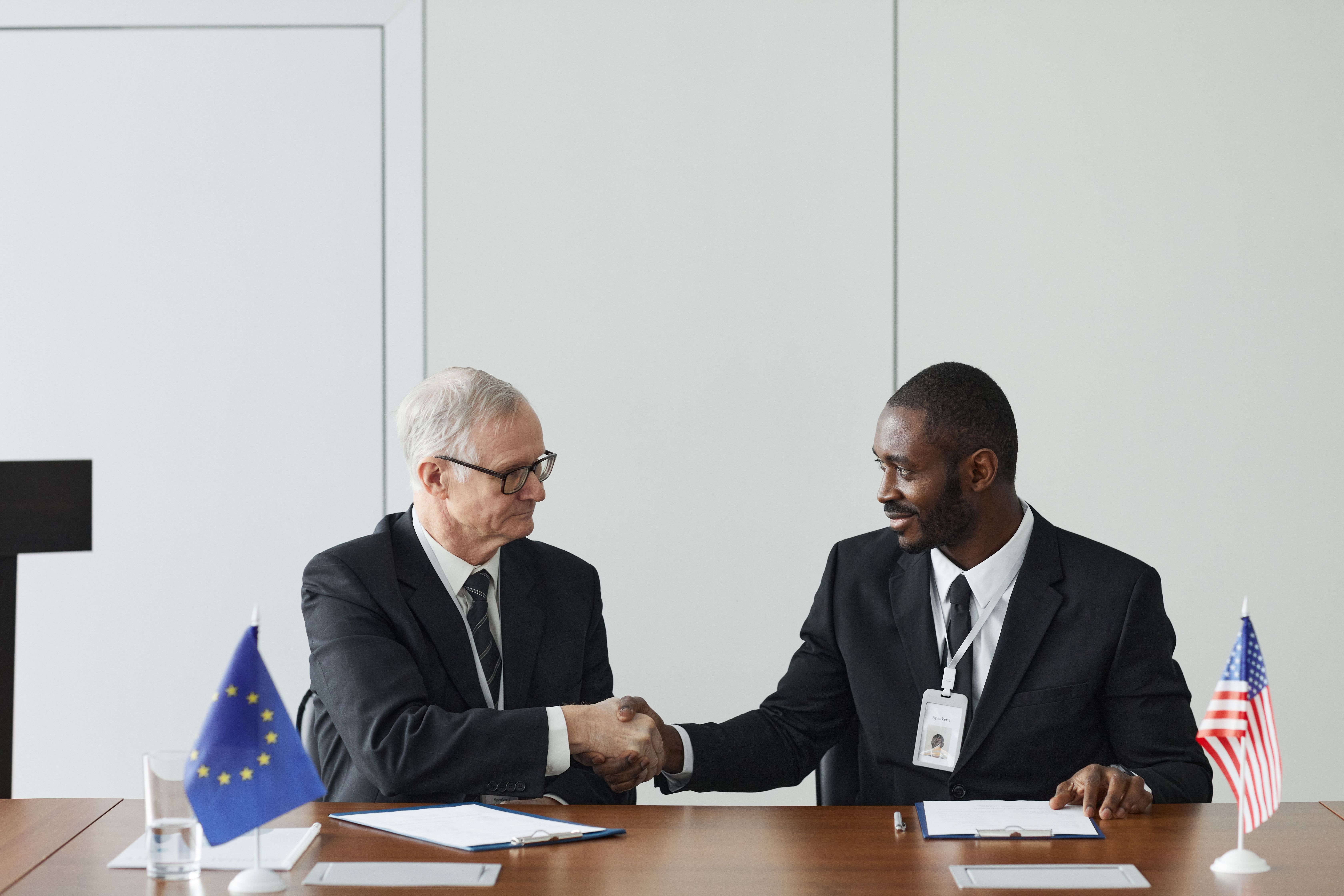 Corporate handshake between businessmen in front of EU and US flags, symbolizing partnership