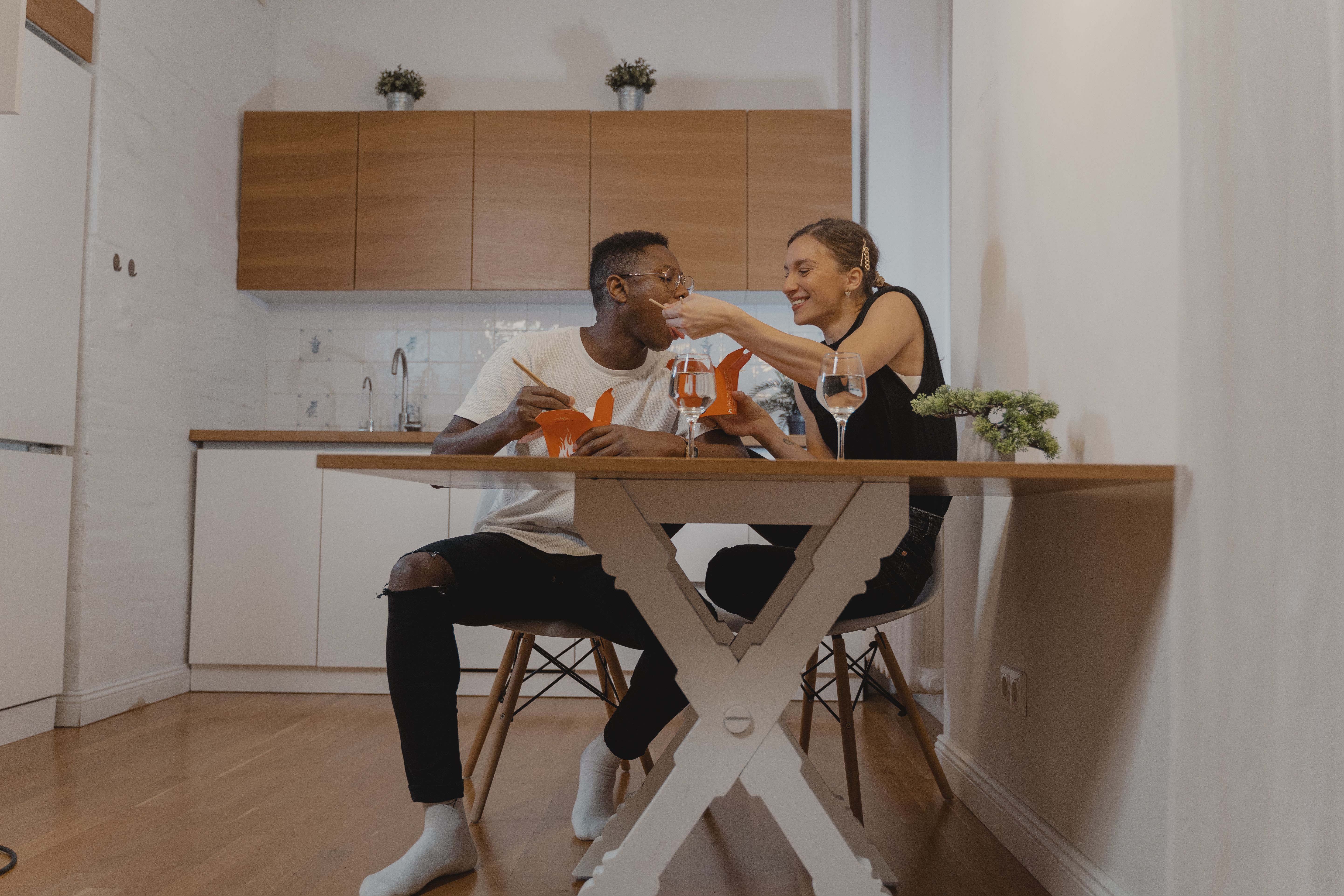 Happy couple enjoying a cozy takeout dinner and wine at home to save money on a date