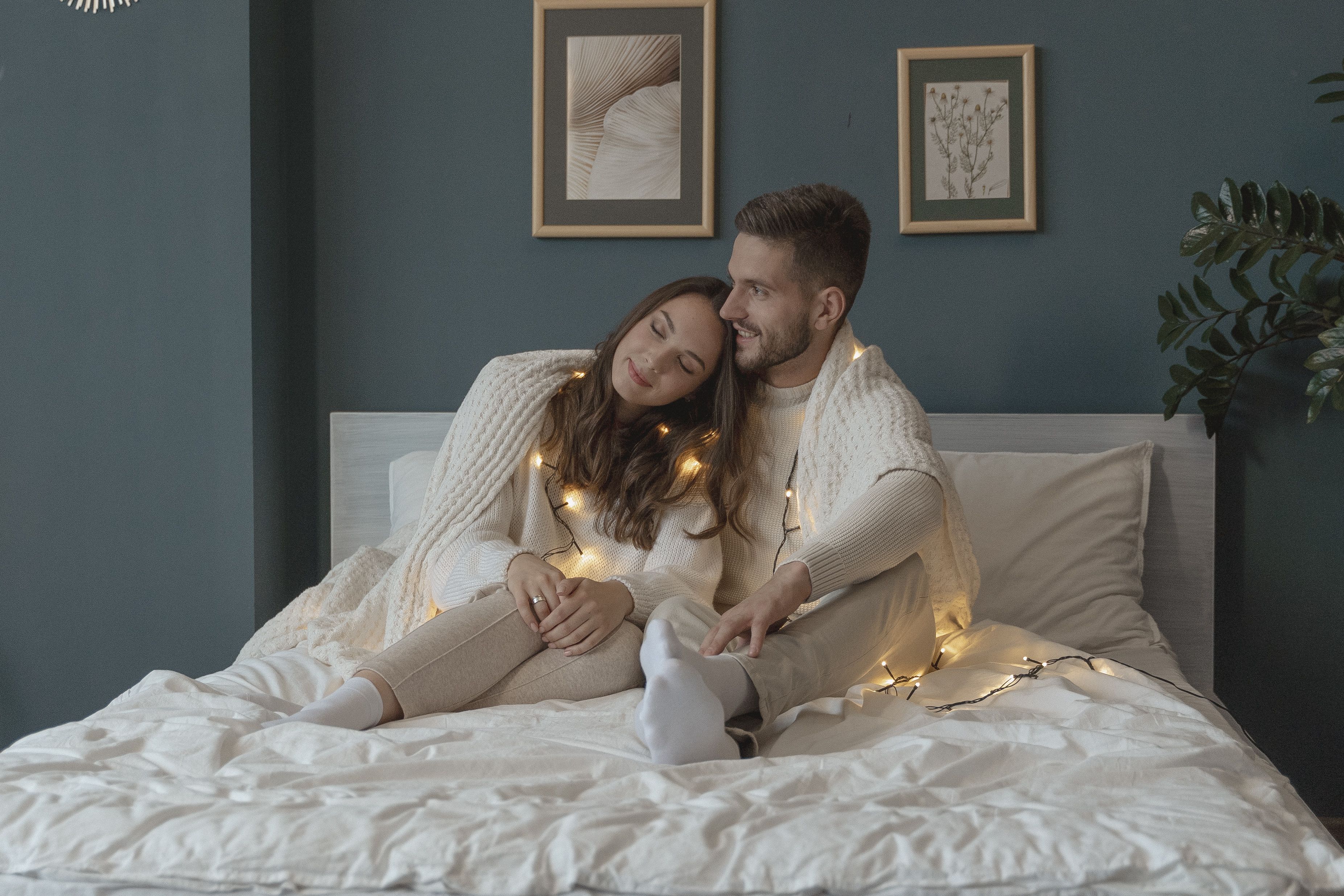 Loving couple cuddling on a bed wrapped in string lights for a cozy free date night