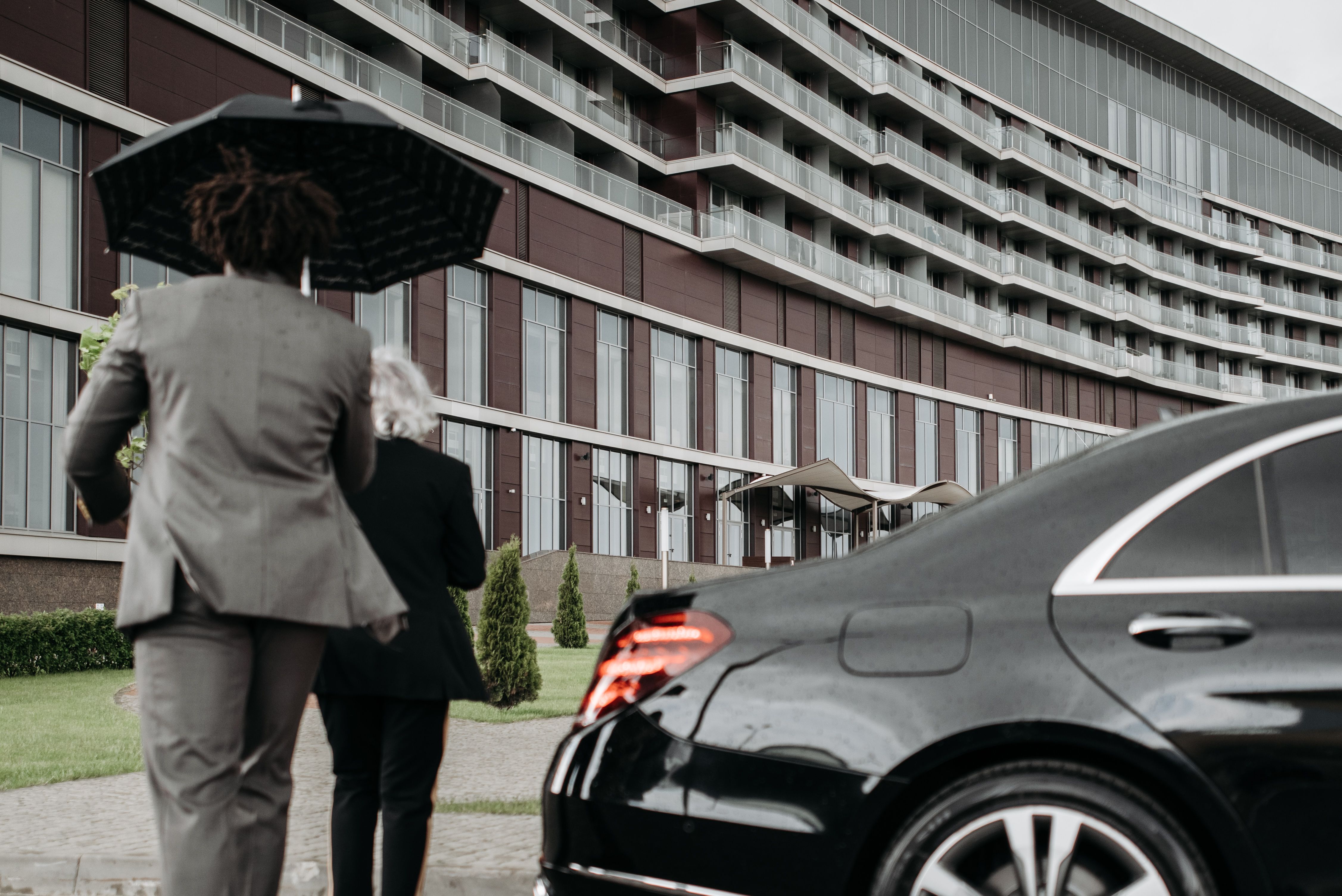 Two suited professionals walking beside a luxury car, suggesting discreet executive protection in daily life.