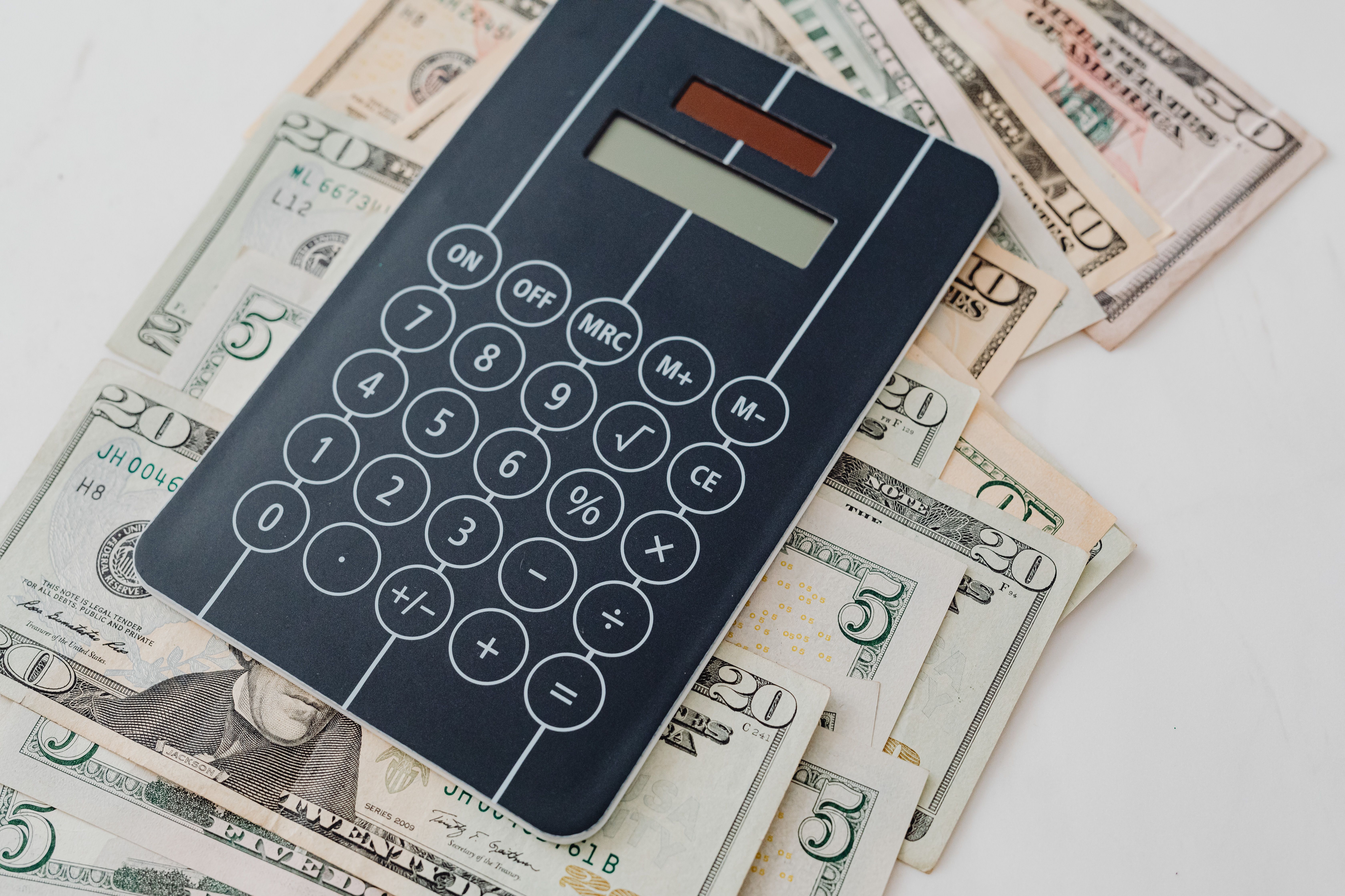 Calculator resting on US dollar bills representing budgeting for expensive legal fees