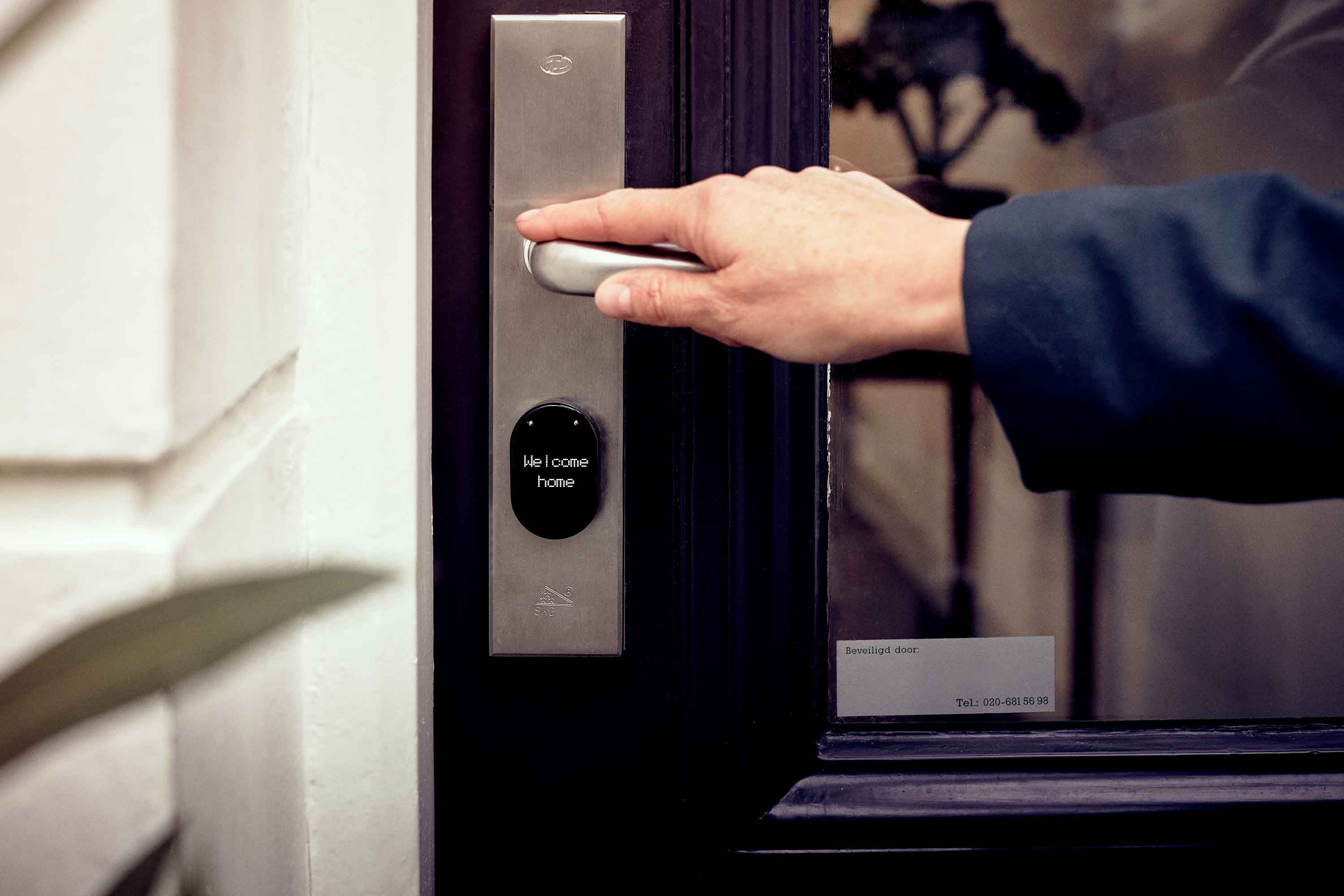 A hand opening a smart home door with a digital access panel, illustrating connected entry security.